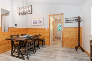 A wooden-paneled room with a dining table, chairs, a bench, a coat rack, and a hallway leading to another room.