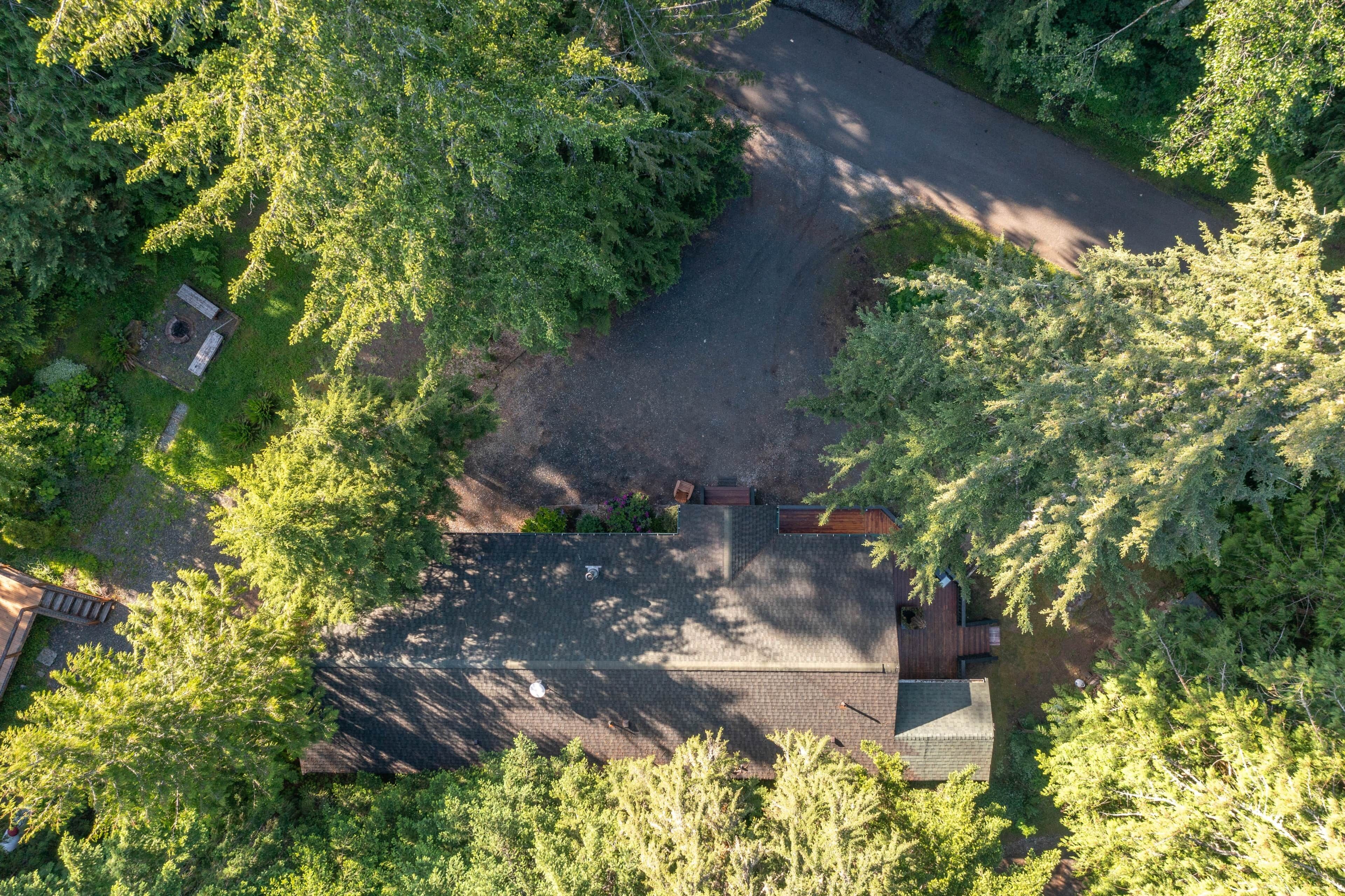 An aerial view of a residential area with a paved driveway, a small fenced yard, and a house with a sloped roof.