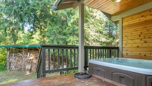 A wooden deck with a hot tub, a stone wall, and a covered area with a green roof.