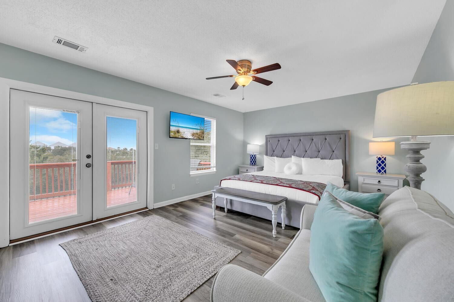 A bedroom with a bed, a ceiling fan, a nightstand, a lamp, a bench, and a view through the sliding doors.