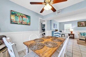 A dining area with a wooden table, white chairs, and woven placemats. - Sand Dollar A (Panama City Beach)