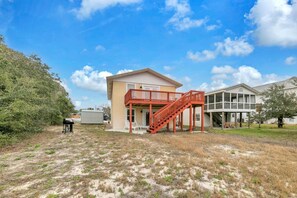 A two-story house with a red staircase leading to a balcony, surrounded by dry grass and trees. - Sand Dollar A (Panama City Beach)