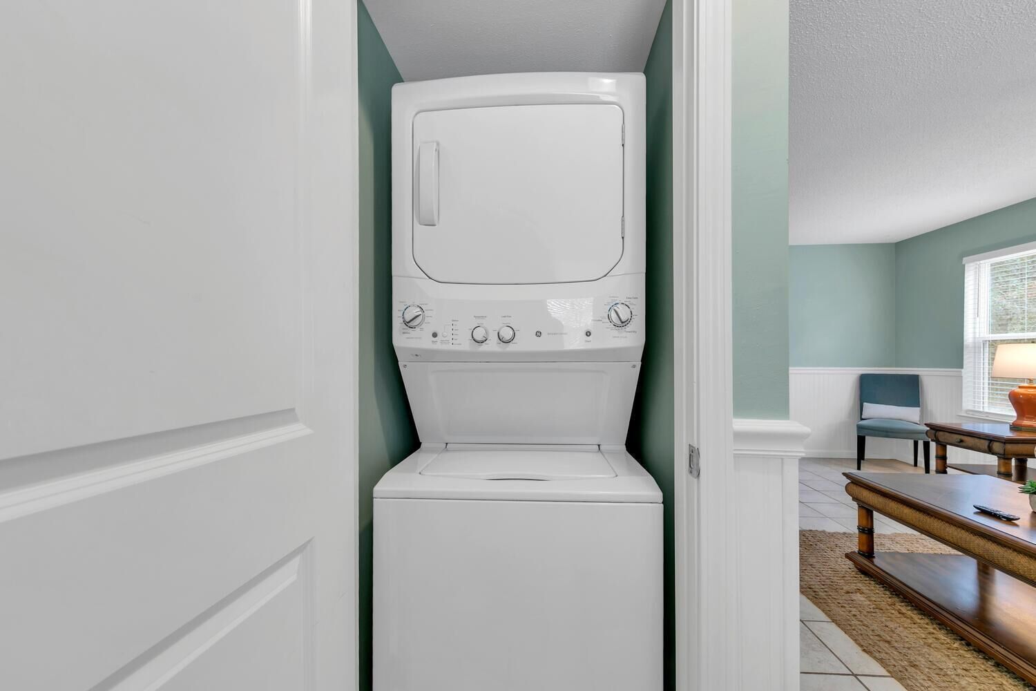 A compact, white front-loading washer and dryer unit in a narrow hallway with teal walls.