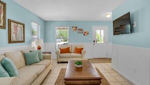 A living room with a beige sofa, a striped armchair, a wooden coffee table, and a television mounted on the wall.