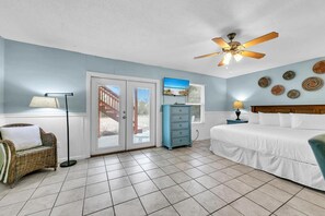 A bedroom with a bed, a dresser, a ceiling fan, and a view through the glass doors. - Sand Dollar A (Panama City Beach)
