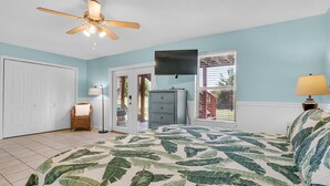 A bedroom with a bed, a ceiling fan, a dresser, a television, and a window with blinds.