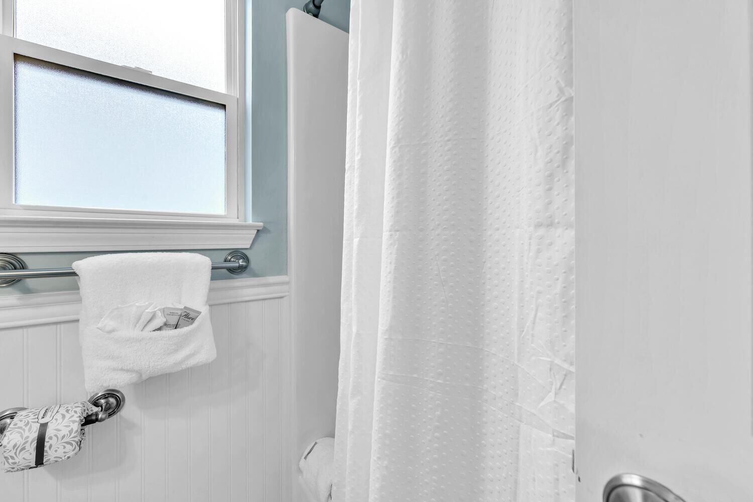 A bathroom with a white towel hanging on a metal towel rack, a shower curtain, and a window with a view of the sky.
