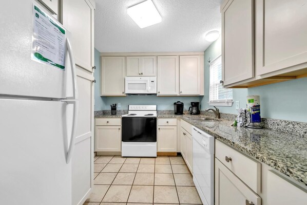 A kitchen with white cabinets, a stove, a microwave, and a granite countertop. - Sand Dollar A (Panama City Beach)