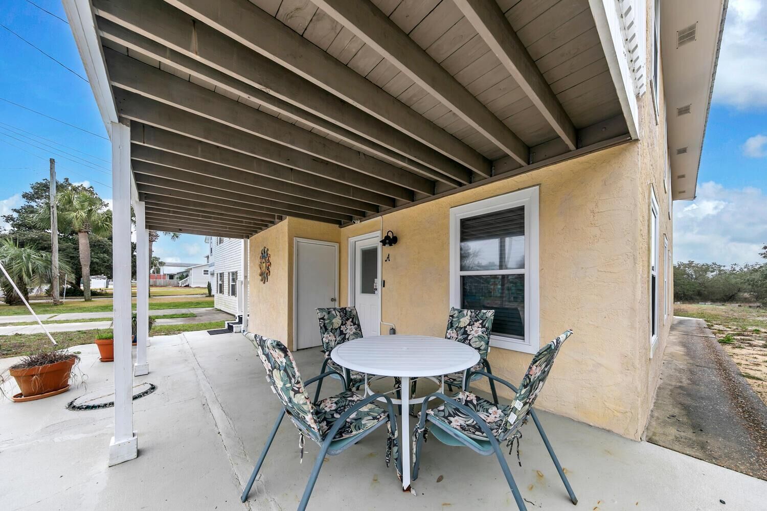 A covered patio with a round table and chairs, a door, and a window.