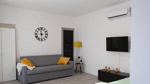A modern, well-lit room with a grey sofa, a black TV, and a wall clock. - ✨Relax at Lake Garda – Free Wi-Fi, Private Garden (Lombardia)