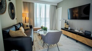 Un salon moderne avec un canapé en cuir noir, un fauteuil gris, une table basse et un téléviseur fixé au mur.