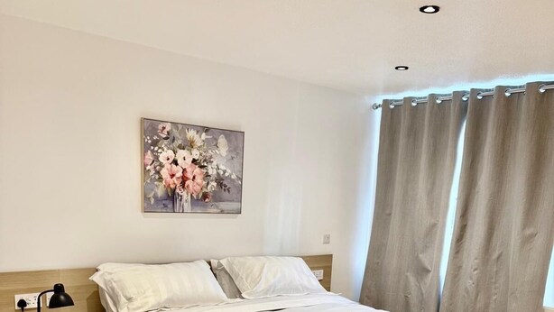 A neatly arranged bedroom with a bed, bedside table, lamp, and a painting on the wall.
