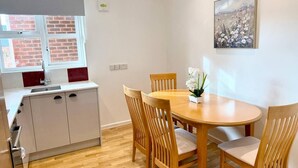 A compact kitchen with a window, a dining table with chairs, and a painting on the wall.
