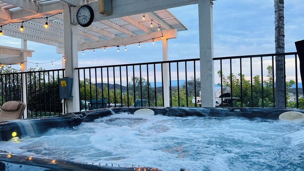 A hot tub with water jets, a clock, string lights, and a view of mountains.