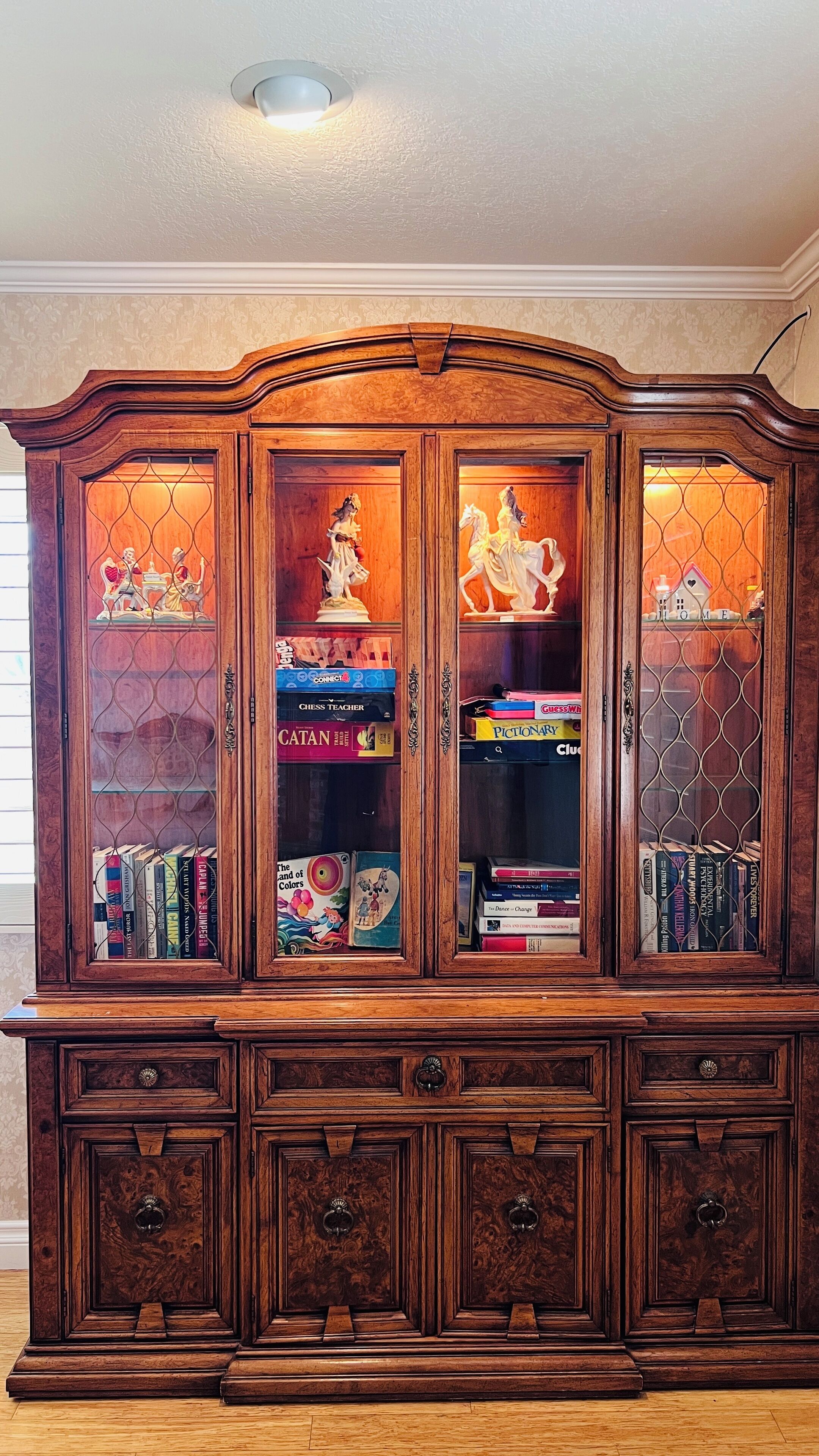 A wooden bookcase with glass doors, containing books and decorative items.