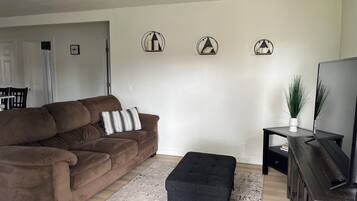 Een woonkamer met een bruine bank, een zwart voetenbankje, een tv-meubel en een vloerkleed.