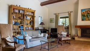 A living room with a sofa, chairs, a coffee table, a bookshelf, a piano, and a fireplace.