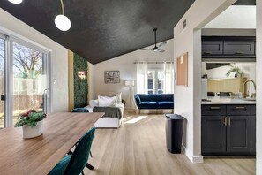 A modern living space with a dining area, a sofa, a ceiling fan, and a kitchen with dark cabinets.