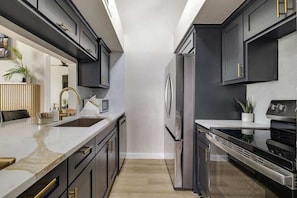 A modern kitchen with dark cabinetry, stainless steel appliances, and a marble countertop.