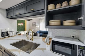 A kitchen with a white countertop, a stainless steel sink, a microwave, and dark cabinets.