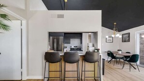 Una cocina moderna con una isla central, taburetes de bar y un comedor con mesa y sillas.