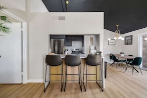 A modern kitchen with a central island, bar stools, and a dining area with a table and chairs.
