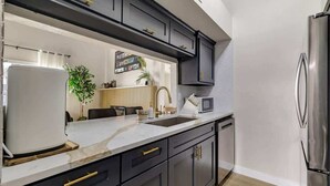 Una cocina moderna con gabinetes oscuros, un refrigerador de acero inoxidable, una encimera blanca y un horno empotrado.