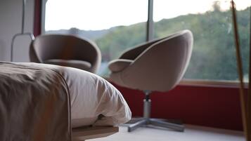 Un dormitorio con cama, una silla y un ventanal que ofrece vistas a zonas verdes.