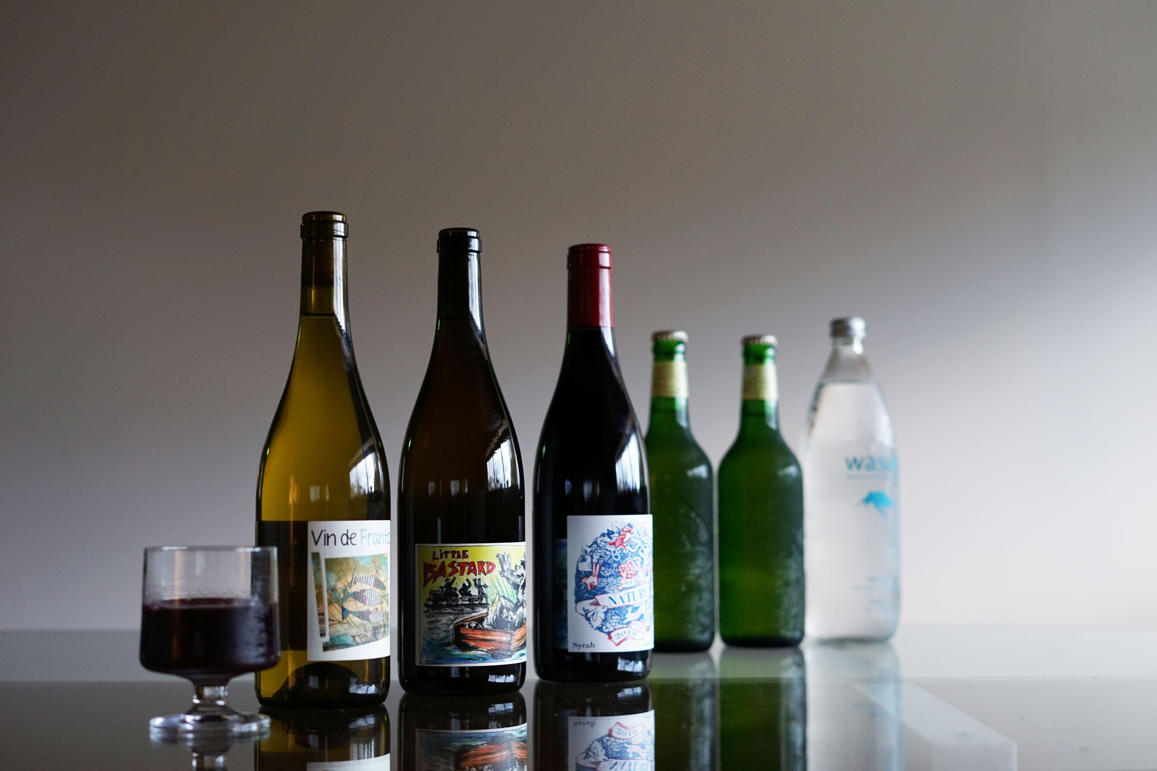 A selection of wine bottles and a glass of red wine on a reflective surface.