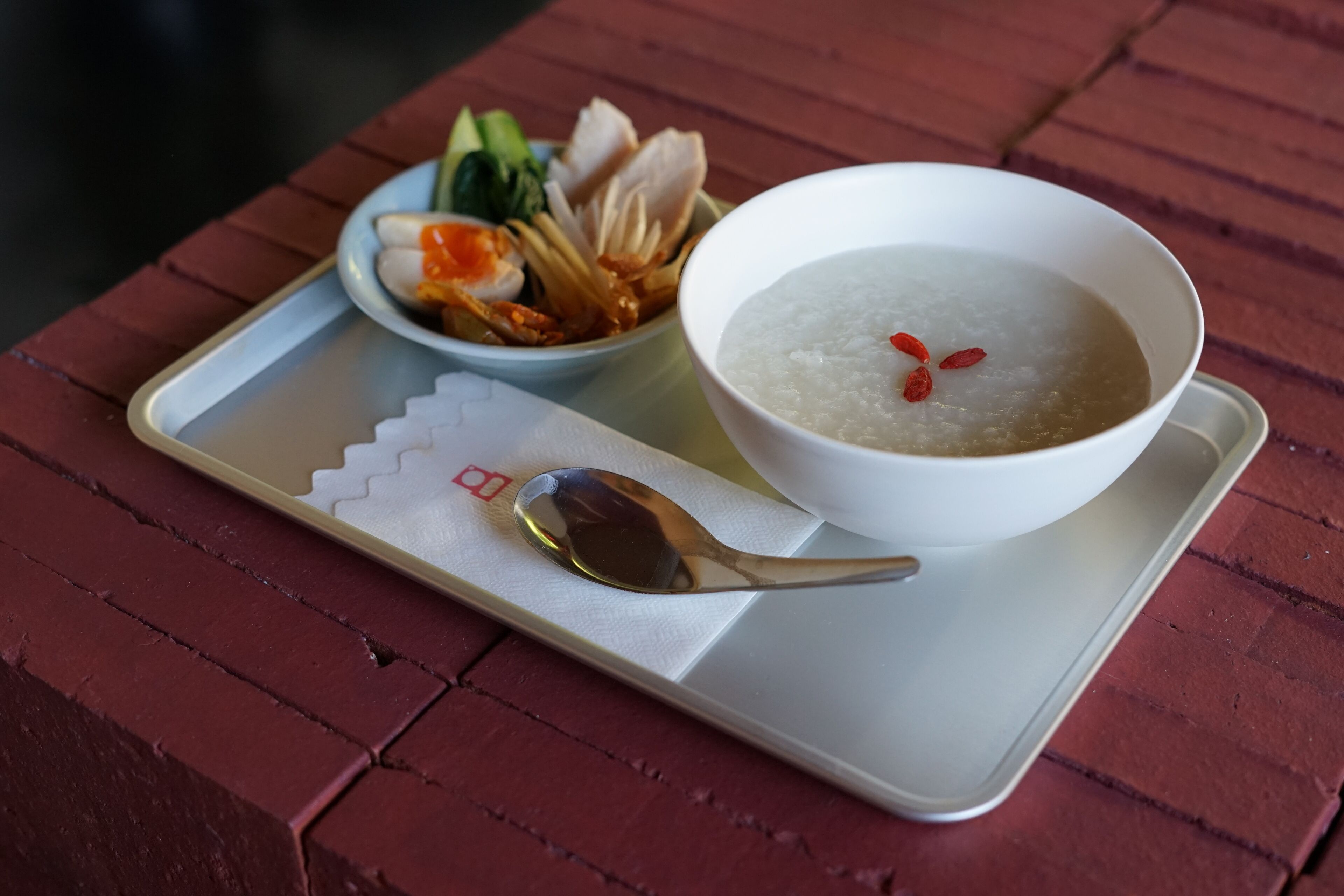 A tray with a bowl of rice porridge, a spoon, and a plate of vegetables and meat.