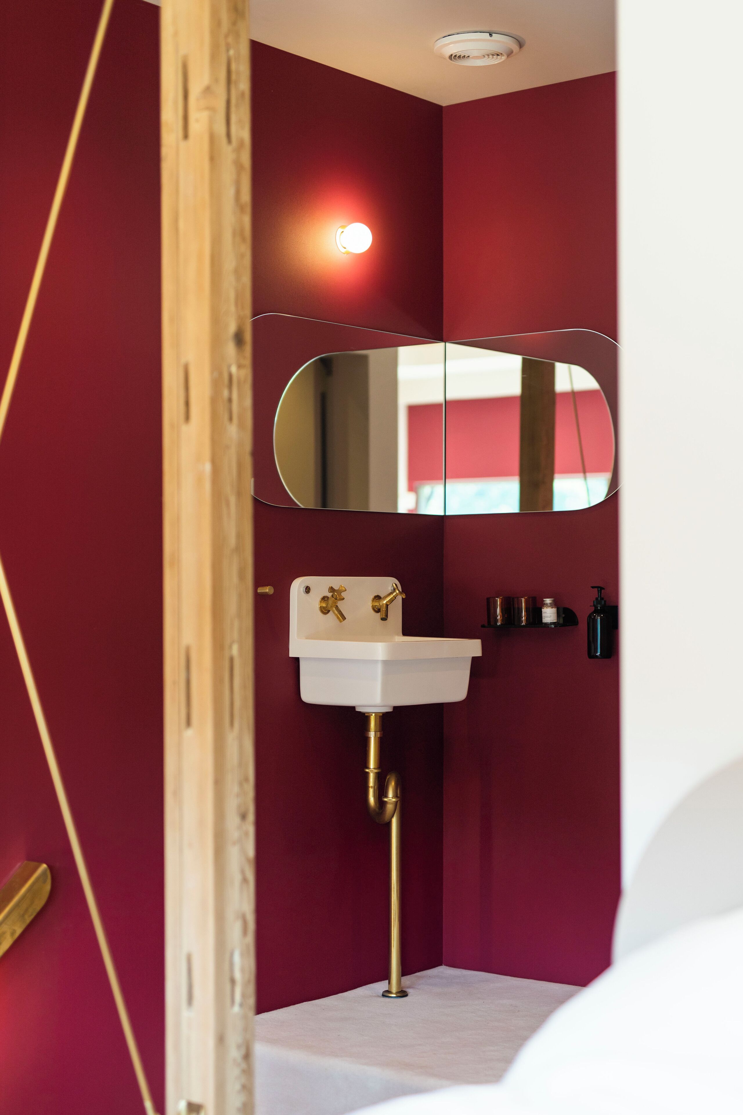 A bathroom with a white sink, a gold faucet, a mirror, and a red wall.