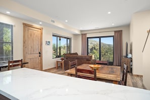 Amplia sala de estar con una gran mesa de comedor de madera, un sofá y vistas al exterior a través de amplias ventanas.