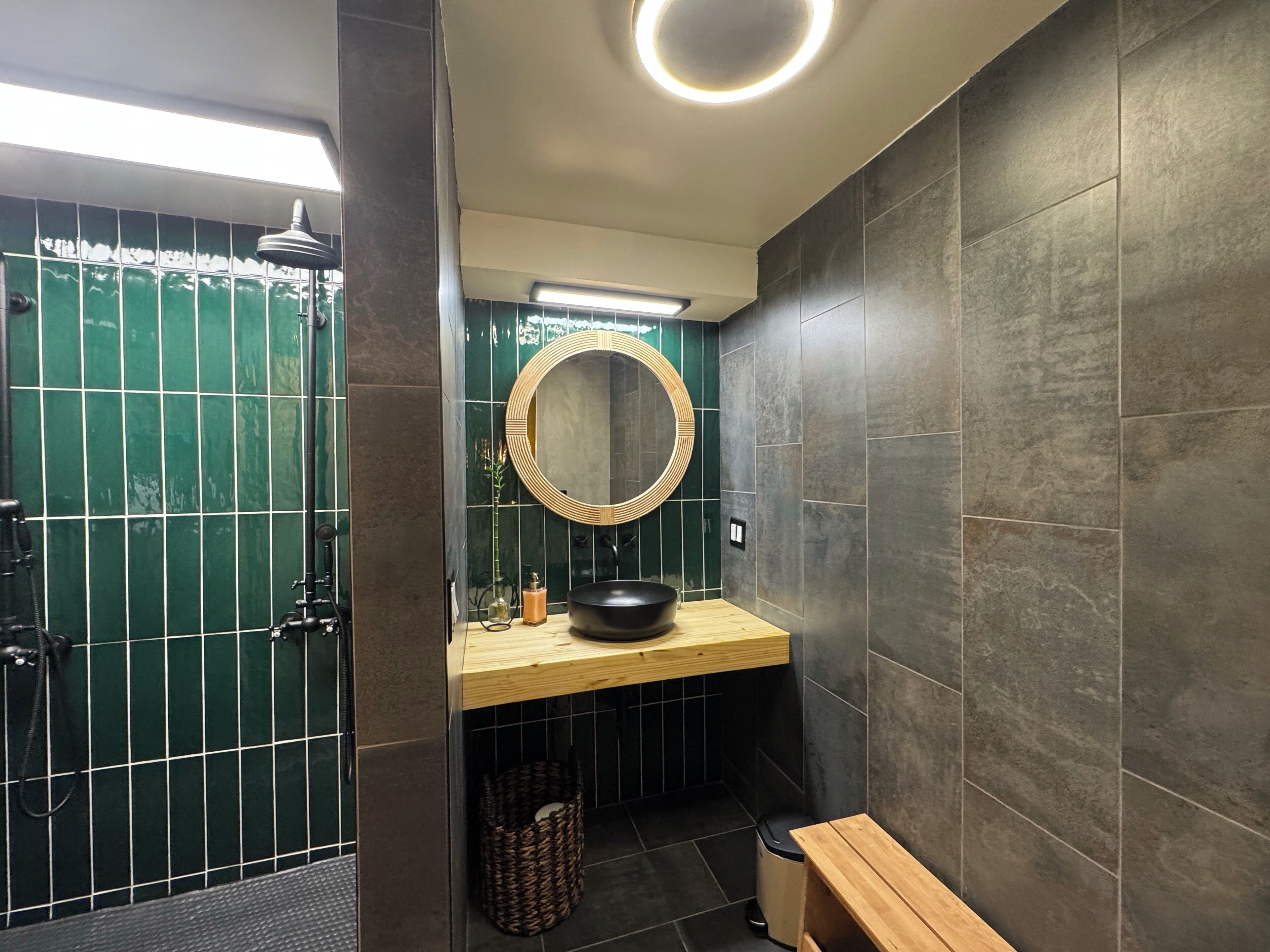 Een moderne badkamer met een houten wastafel, een ronde spiegel en een zwarte wasbak.