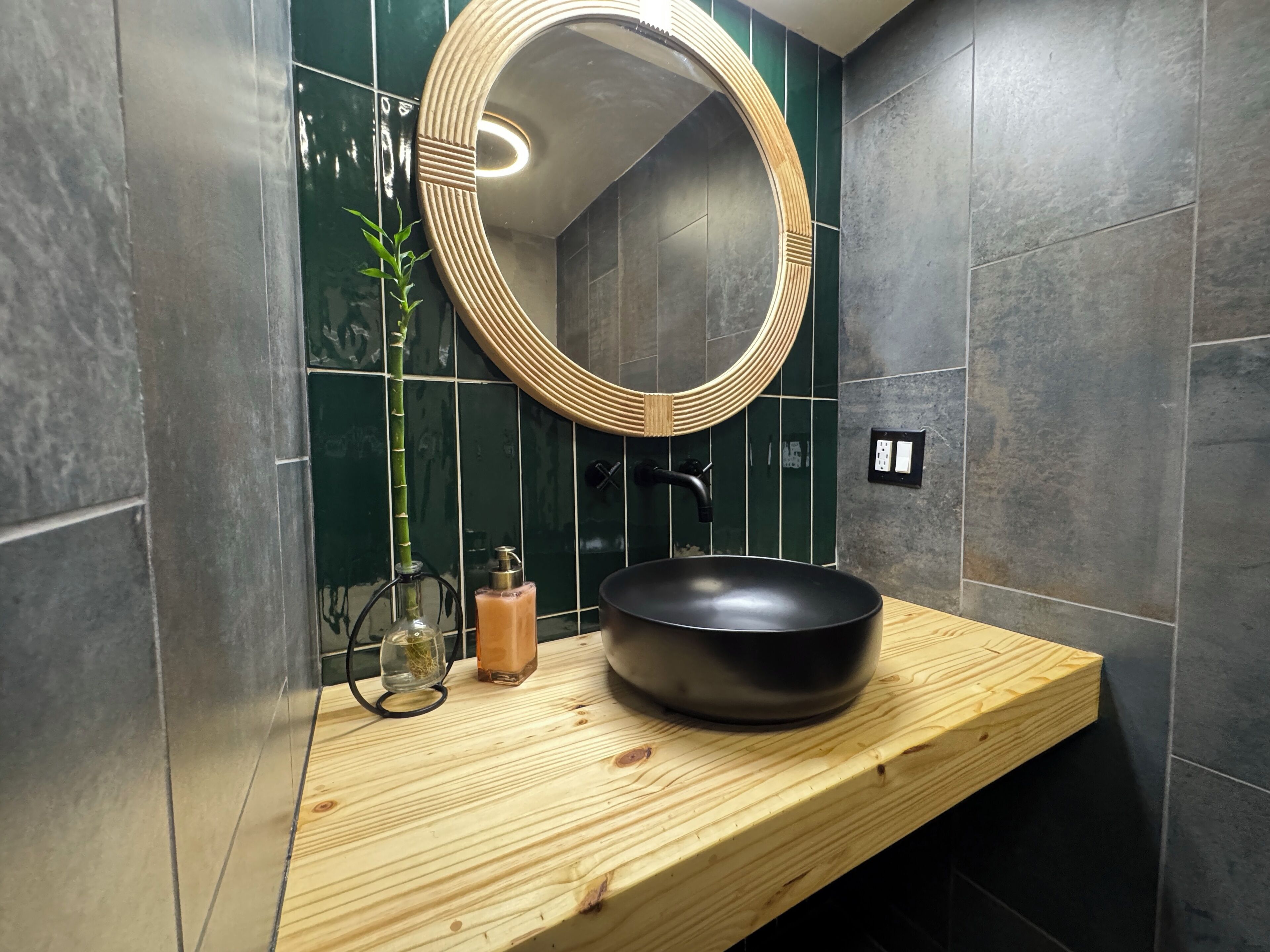 A bathroom with a wooden vanity, a black sink, a round mirror, and a green plant.