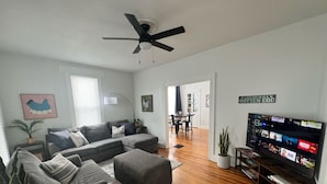 Una sala moderna con un sofá modular, un televisor de pantalla plana y un ventilador de techo.