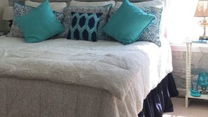 Ein Schlafzimmer mit einem Bett, gemusterten Kissen, einem Holz-Kopfteil und einem Fenster mit Vorhängen.
