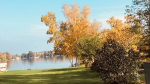 Blick auf einen See mit Herbstlaub, eine Rasenfläche und ein Picknicktisch.