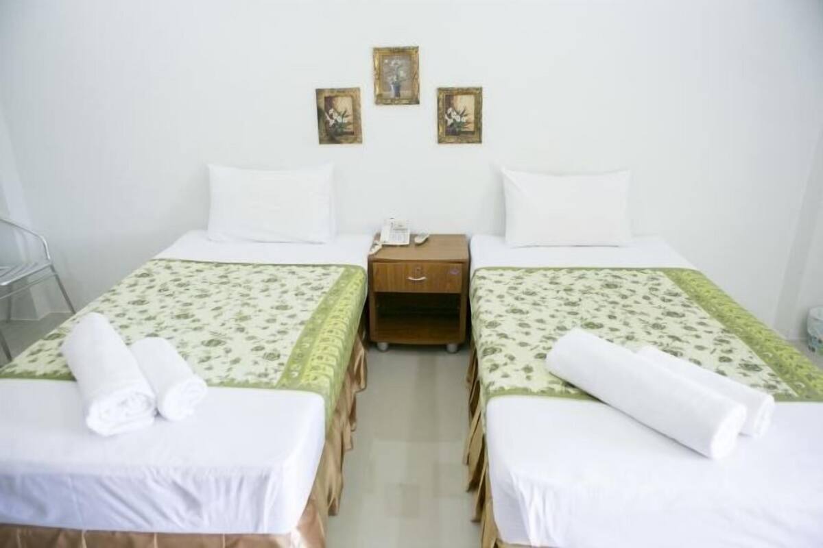 A hotel room with two beds, a nightstand, and three framed pictures on the wall.