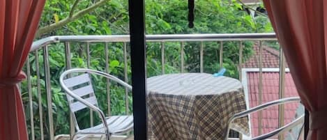 A balcony with a table and chairs, surrounded by a metal railing, and overlooking a garden.
