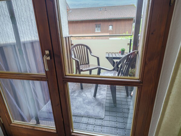 A view through a glass door to an outdoor patio area with a wooden table, two chairs, and a small potted plant. - Comfortable, bright 2-room apartment (Waldkirchen)