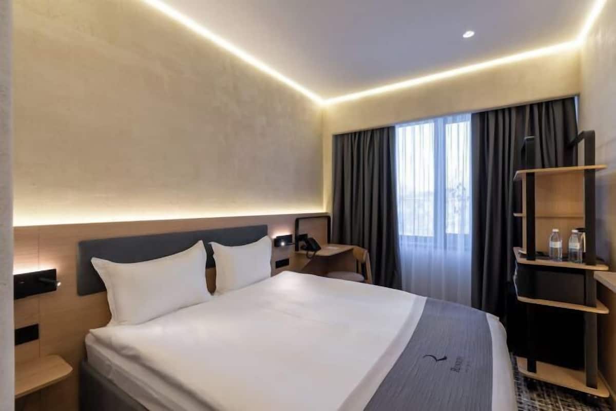 Une chambre d’hôtel avec un lit, des tables de chevet, un bureau, une chaise, une télévision et une fenêtre avec des rideaux.