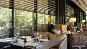 Un ristorante con tavoli apparecchiati, sedute imbottite e ampie finestre che si affacciano sul verde.