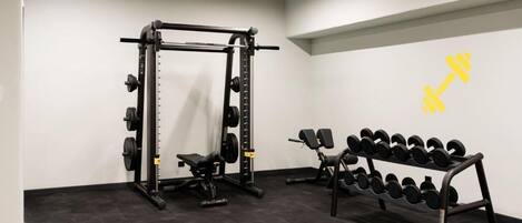 A gym with a squat rack, bench, dumbbells, and a weight plate rack.