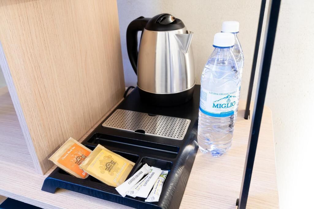 Una cafetera, una botella de agua y una bandeja con cápsulas de café y un sobre de leche condensada sobre una superficie de madera.
