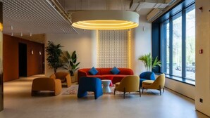 Una hall moderna con un divano rosso, poltrone blu e gialle, un tavolino da caffè bianco e un'ampia finestra che lascia entrare la luce naturale.