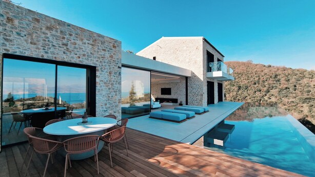 A modern house with a stone exterior, a pool, and a dining area with outdoor seating. - Luxury Villa with Infinity Pool & Sea Views in Northeast Corfu (kassiopi)