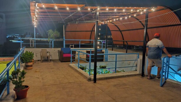 An outdoor patio area with a covered seating area, potted plants, and a view of a sports field. - Believer Hostel (Santa Marta)