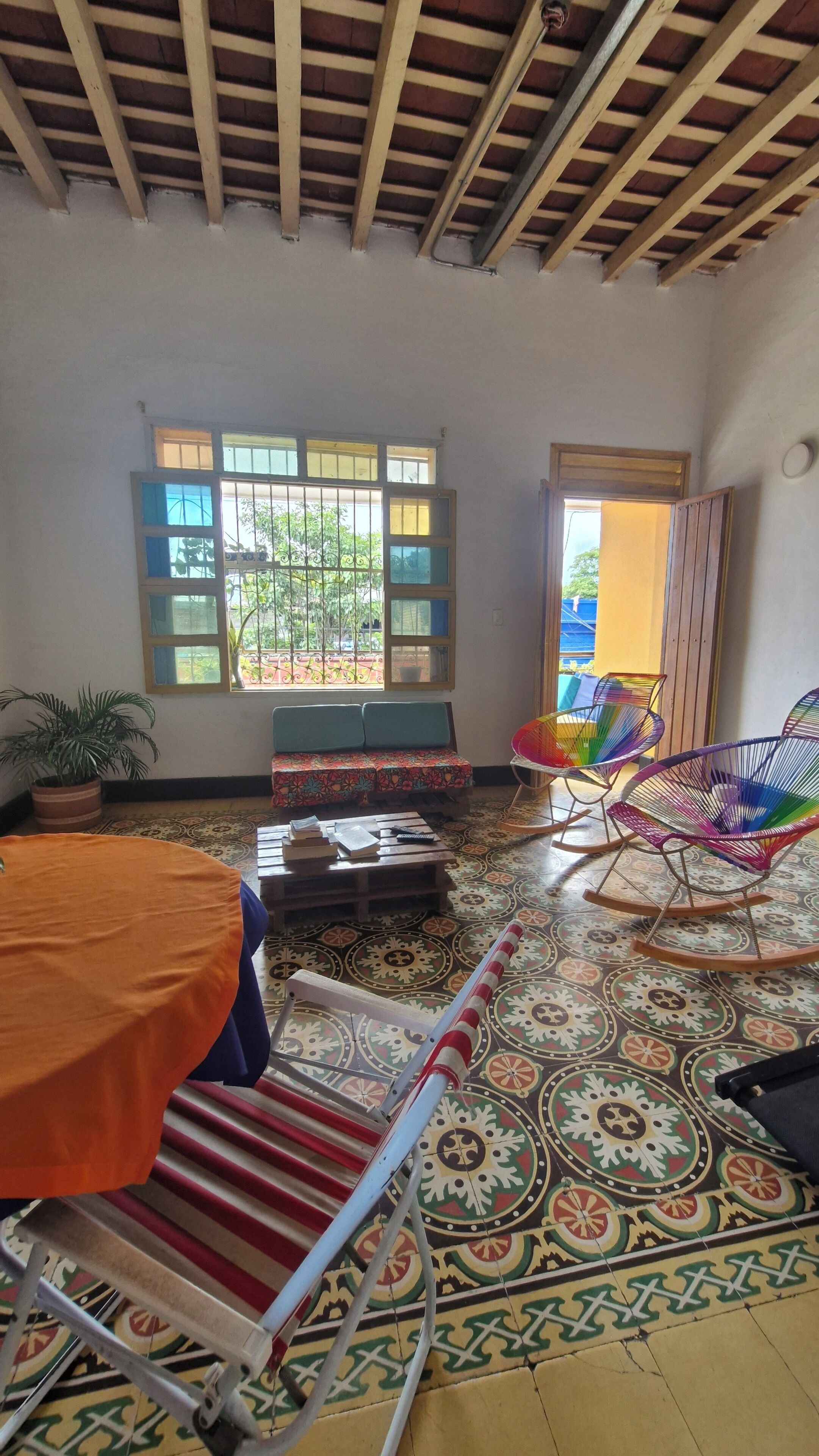 A room with a wooden ceiling, a bench, colorful chairs, a patterned floor, and a window with bars.