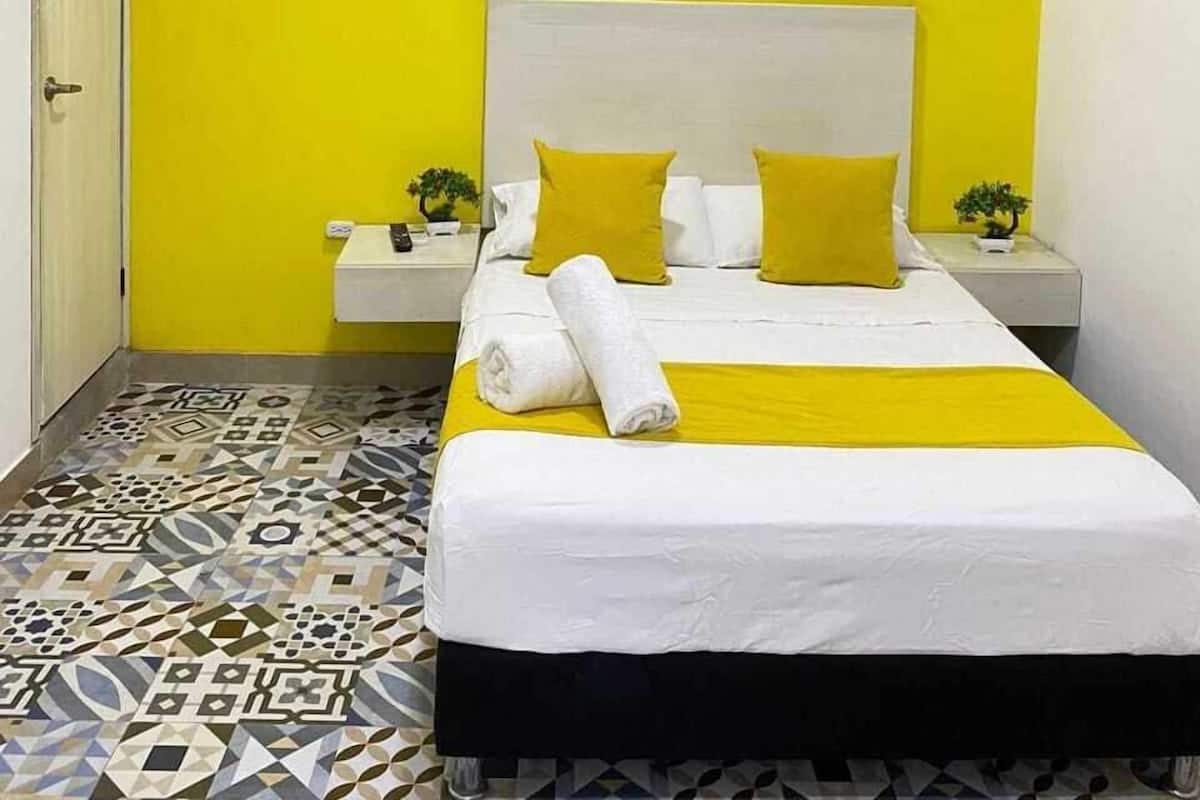 A hotel room with a bed, a nightstand, a wall-mounted air conditioner, and a patterned floor.