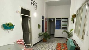 A spacious indoor area with patterned floor tiles, a glass table with chairs, a sofa with colorful cushions, and potted plants. - Believer Hostel (Santa Marta)